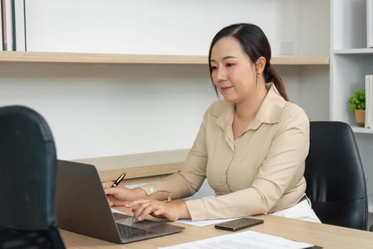 A businesswoman concentrates on her laptop, showcasing dedication and productivity in a contemporary workspace.