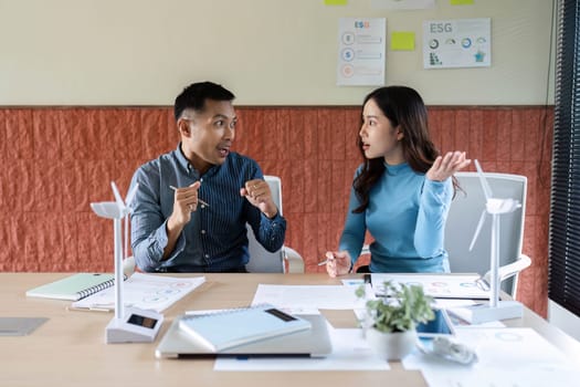Two colleagues animatedly discuss ESG strategies, reviewing documents and sharing insights in a bright office environment.