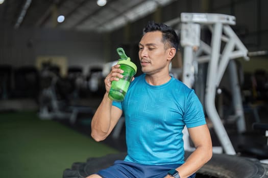 A fit man enjoys a sip from his protein shaker, highlighting the importance of hydration during fitness routines.