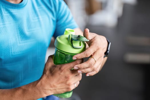 A close-up of a man holding a green shaker bottle, emphasizing hydration and fitness. The image captures a moment of preparation for a workout.