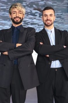 Two confident male professionals in suits standing with crossed arms, smiling at the camera inside a modern office. Corporate success, teamwork, and leadership in business environment. Vertical