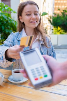 Caucasian woman smiling as she pays with a credit card using contactless technology at an outdoor cafe. A casual urban moment reflecting convenience, lifestyle, and modern financial habits. Vertical