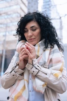 Caucasian woman enjoys a warm drink from a red cup while standing outdoors. She wears a soft scarf and light jacket, suggesting a cool day. Calm and cozy moment captured in natural daylight. Vertical