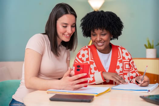 Caucasian and African American friends share a joyful moment as they look at a mobile phone together. Their smiles and relaxed vibe highlight connection, friendship, and digital engagement indoors.