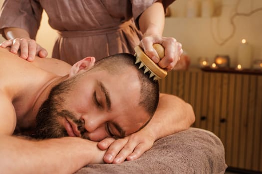 Male client experiences calming scalp massage using a brush tool in a peaceful spa. Promotes relaxation and head tension relief.