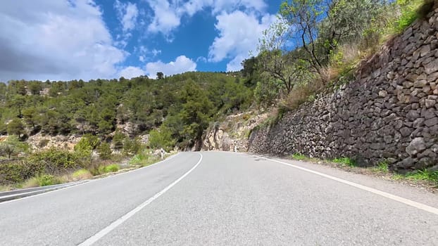A beautiful winding road is surrounded by vibrant greenery and rocky walls under a partly cloudy sky
