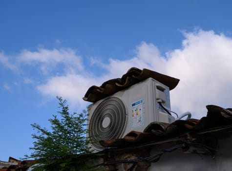 An outdoor air conditioning unit installed on a house roof, uniquely covered with matching clay tiles for aesthetic and protection. Cyprus residential design.