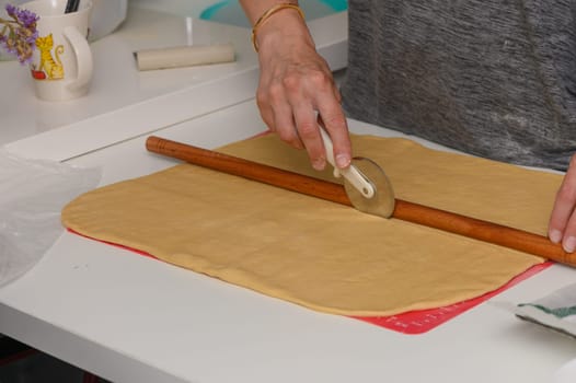 A woman slices dough into even portions using a pizza cutter, preparing it for baking.