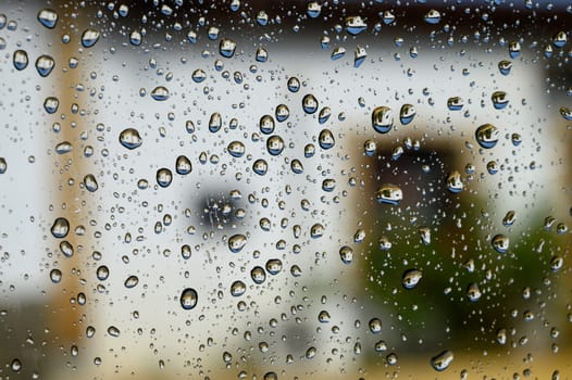 Water droplets on a car window glass after rain, creating a natural abstract texture with soft light and blurred background.