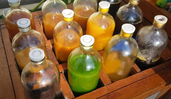 Colorful Bottles of traditional natural organic medicine locally called jamu, Displayed in Wooden Case on a Sunny Day, Various colorful bottles filled with liquids arranged in a wooden container outdoors under sunlight.