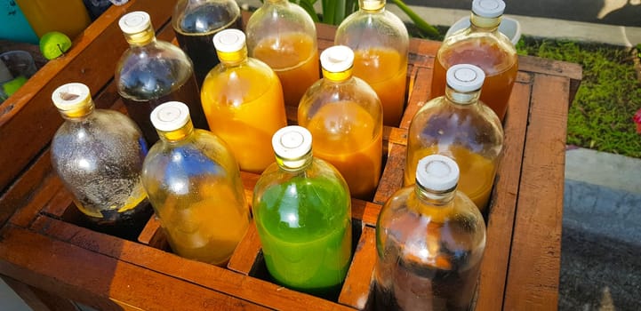 Colorful Bottles of traditional natural organic medicine locally called jamu, Displayed in Wooden Case on a Sunny Day, Various colorful bottles filled with liquids arranged in a wooden container outdoors under sunlight.