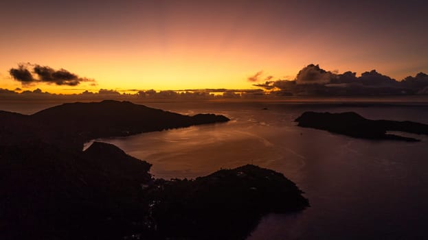 A fiery sunset bathes the horizon in warm light, while the islands and water rest in shadows. Praslin, Seychelles.