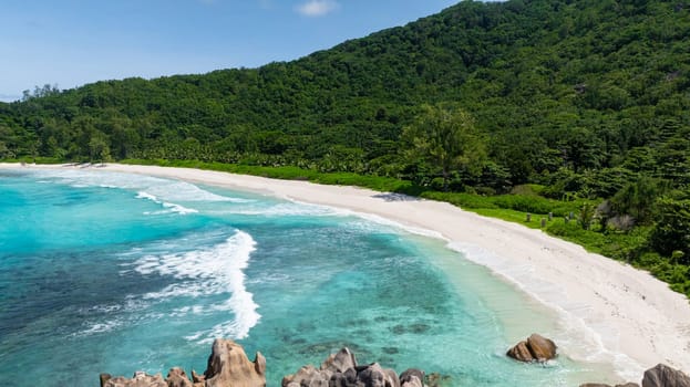 A pristine tropical beach with turquoise waves and white sand, surrounded by lush greenery. Anse Cocos. Seychelles, La Digue.