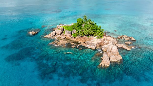 An island surrounded by turquoise ocean waters with prominent granite formations and lush greenery. Seychelles, Praslin.