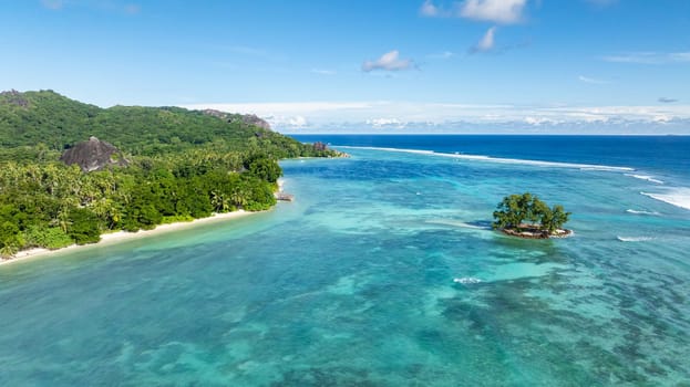 A small island surrounded by clear turquoise water near a pristine sandy beach. La Digue, Seychelles.