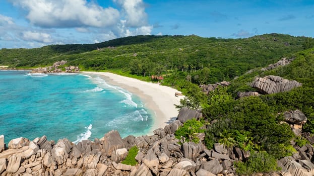 A turquoise beach surrounded by lush greenery and large rocky formations. Grand Anse Beach, La Digue, Seychelles.