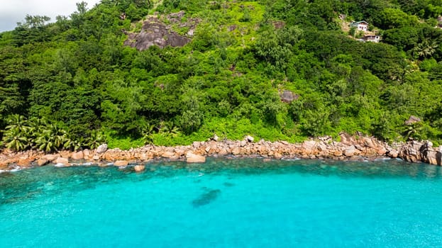 The vibrant meeting of turquoise waters and rugged rocky shores flanked by dense greenery. Praslin, Seychelles.