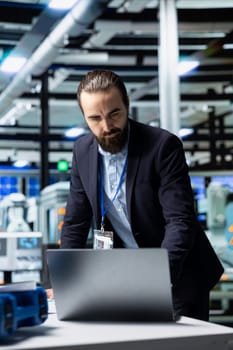 Facility supervisor in a suit monitoring solar panel production line, reflecting professional occupation and executive level involvement in renewable energy development. Solar power.