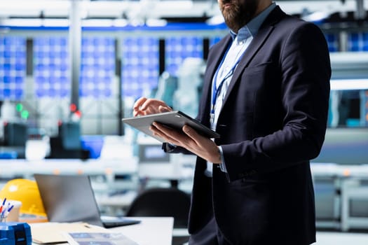 Quality control analyst in a solar manufacturing plant evaluates workflow, dressed in suit to reflect corporate oversight and business leadership. Technical knowledge in sustainable energy.