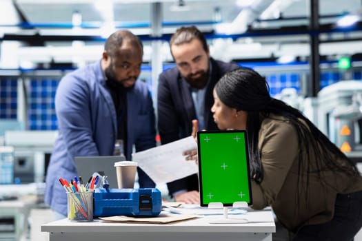 Solar panel diverse group reviewing insight on pc next to green screen, finding errors during a process audit and helping optimize renewable energy operations. Photovoltaics factory.