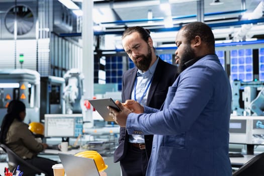 Multiethnic specialists engineers doing teamwork on modern production line for solar panels power, combining technical insight and collaboration for renewable energy infrastructure.