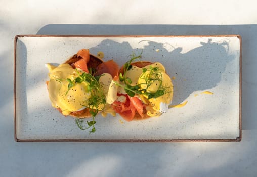 Top view of Eggs Royale made with english muffin, oak smoked salmon, a brace of poached hen's eggs & hollandaise sauce and watercress served on blue ceramic tray. use it as your Wallpaper, Poster and Copy space, Selective focus.