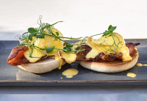Eggs Benedict made with english muffin, grilled bacon, a brace of poached hen's eggs & hollandaise sauce and watercress served on ceramic tray. use it as your Wallpaper, Poster and Space for text, Selective focus.