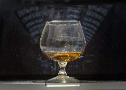 Whiskey glass or Brandy snifter stands on Laptop with laptop screen in the background. use it as your Wallpaper, Poster and Space for text, Selective focus.