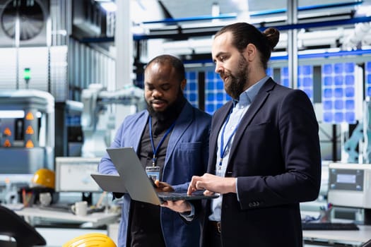 Team of diverse analysts consultants reviewing data and checklists in a high tech solar panel plant, ensuring manufacturing process meets sustainable energy and innovation standards.