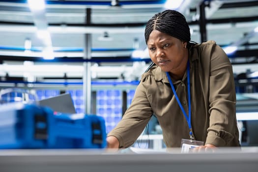 Female plant consultant examines production insight on laptop, ensuring efficiency and professionalism in the solar power facility. Working on renewable energy success for industrial operations.