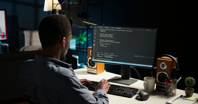 African american expert at desk using pc for programming and data analysis. Young networking expert working from his home setup, manages information technology and data center. Camera A.