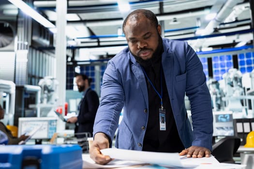 Black male sustainability consultant in suit evaluates solar panel systems and the production line in a modern factory, guiding operations toward clean energy and industrial efficiency.
