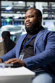 African american male supervisor observes production systems on a pc in a solar plant, providing expert feedback on efficiency, safety and sustainability aligned with green energy initiatives.