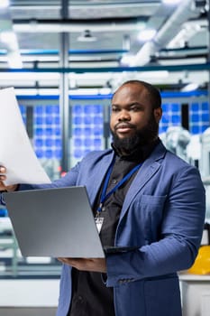 Factory employee checking solar panel machinery and reviewing a checklist, playing a vital role in renewable energy production and assembly line. Efficient solar tech infrastructure.