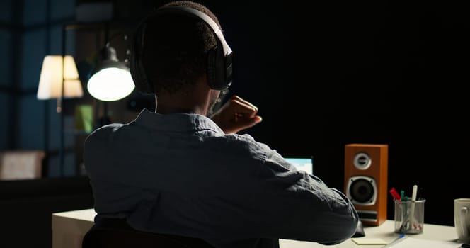African american analyst works on accounting analysis while he is dancing, feeling the rhythm and checks financial balance. Remote worker listening to favorite groovy music on headphones. Camera A.