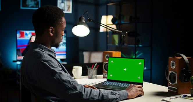 Black man creating a report with data next to isolated chroma key display, improving his skills and achieving career independence. Remote worker solving daily freelance tasks. Camera A.