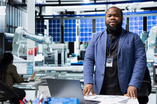Black industrial engineer in a solar panel plant assesses system performance, playing a crucial role in monitoring efficiency and workplace safety. Renewable power with photovoltaics.