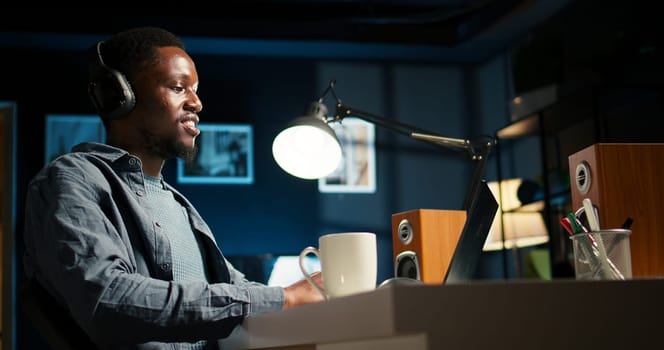 African american guy does remote work and engaging in a web conversation, using his laptop to attend an online video call meeting in his living room. Young man joining a conference. Camera A.