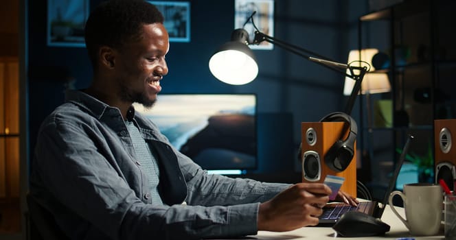 African american guy entering credit card details on internet page, preparing to pay on online clothes shop. During shopping spree on laptop, young man accepts digital monetary transaction. Camera A.