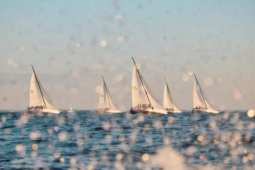 Russia, St.Petersburg, 07 June 2024: Sailing regatta in the Gulf of Finland at sunset, hot race of several yachts, teamwork, yachtsmen sitting on board the boat. High quality photo