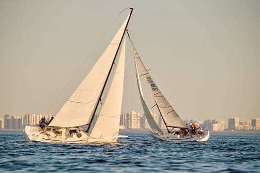 Russia, St.Petersburg, 24 May 2024: Sailing regatta in the Gulf of Finland at sunset, hot race of several yachts, teamwork, yachtsmen sitting on board the boat. High quality photo