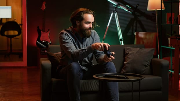 Cheerful gamer rushing home to play newly released game. Happy man jumping on couch, eager to play videogame on console, relaxing after hard day at work, camera A slow motion shot