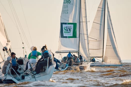 Russia, St.Petersburg, 07 June 2024: Sailing regatta in the Gulf of Finland at sunset, hot race of several yachts, teamwork, yachtsmen sitting on board the boat. High quality photo