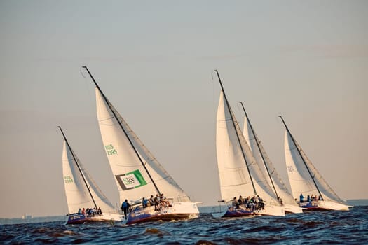 Russia, St.Petersburg, 07 June 2024: Sailing regatta in the Gulf of Finland at sunset, hot race of several yachts, teamwork, yachtsmen sitting on board the boat. High quality photo