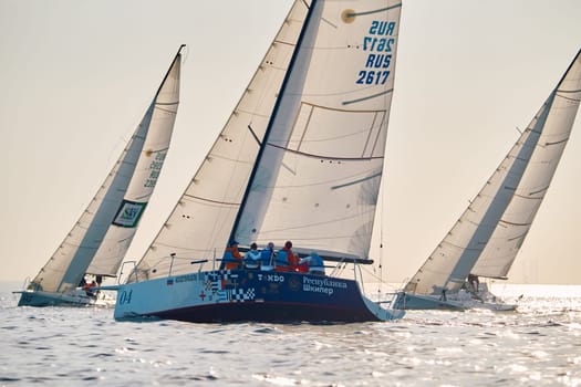 Russia, St.Petersburg, 24 May 2024: Sailing regatta in the Gulf of Finland at sunset, hot race of several yachts, teamwork, yachtsmen sitting on board the boat. High quality photo