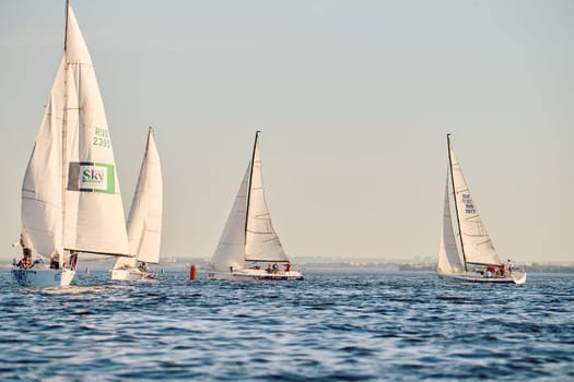Russia, St.Petersburg, 24 May 2024: Sailing regatta in the Gulf of Finland at sunset, hot race of several yachts, teamwork, yachtsmen sitting on board the boat. High quality photo