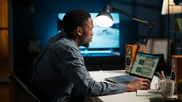 Remote worker organizing project data reviewing his handwritten notes, browsing web for research. Self employed black person managing his freelance job and daily schedule at home. Camera B.