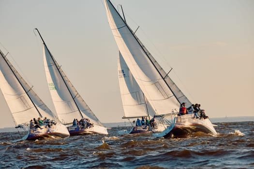 Russia, St.Petersburg, 07 June 2024: Sailing regatta in the Gulf of Finland at sunset, hot race of several yachts, teamwork, yachtsmen sitting on board the boat. High quality photo