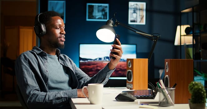 African american man waving and attending a web meeting from his urban apartment. Engaged male freelancer discussing work remotely with coworkers using wireless for video conferencing call. Camera A.