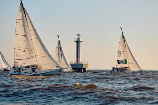 Russia, St.Petersburg, 07 June 2024: Sailing regatta in the Gulf of Finland at sunset, hot race of several yachts, teamwork, yachtsmen sitting on board the boat. High quality photo